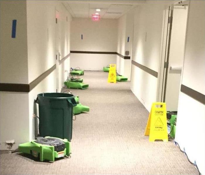 Seven air fans or air movers placed on a long hallway of a building.